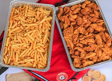 Two trays of food on a table with orange slices.