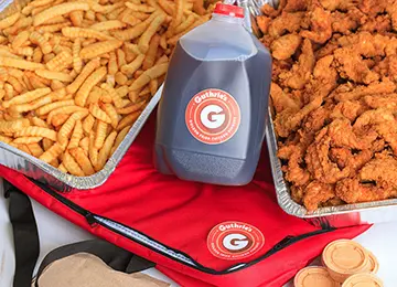 A tray of fried chicken and some fries next to a bottle of sauce.